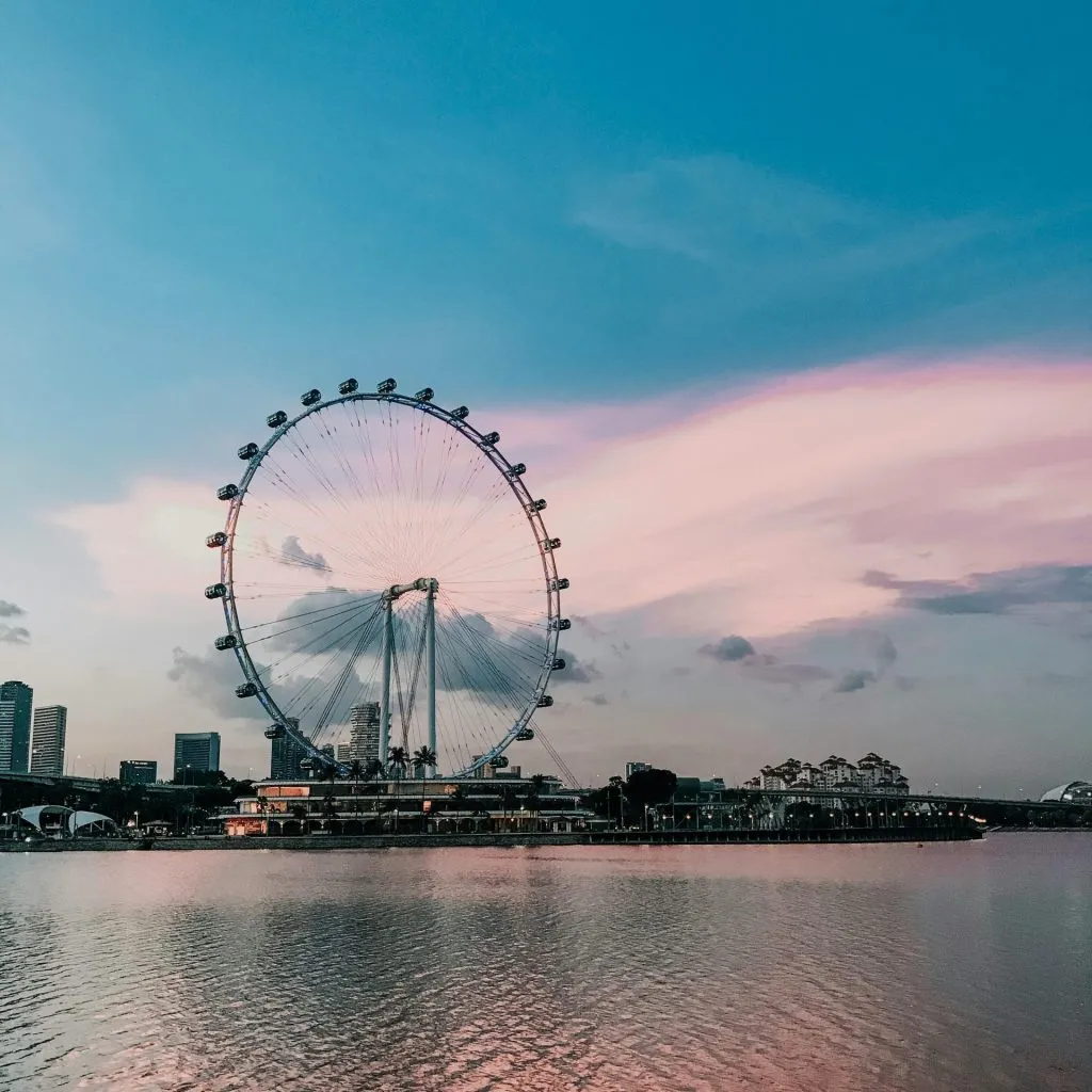 Singapore Flyer at dusk, reflecting on calm waters under a pastel sky.