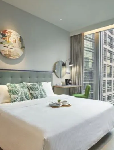A modern hotel room with a cozy bed, green accents, and a large window overlooking a cityscape.