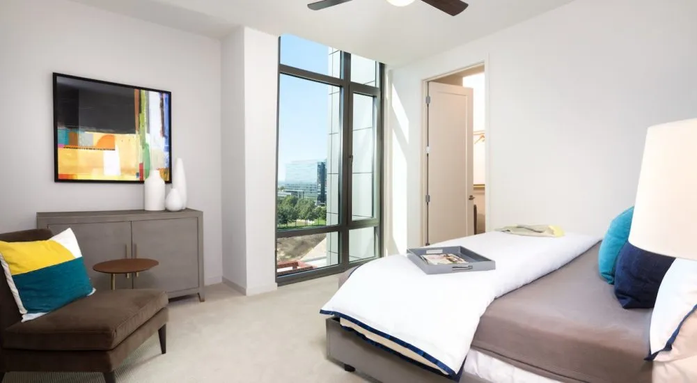 Modern bedroom with large windows, neutral tones, and colorful accents in decor.