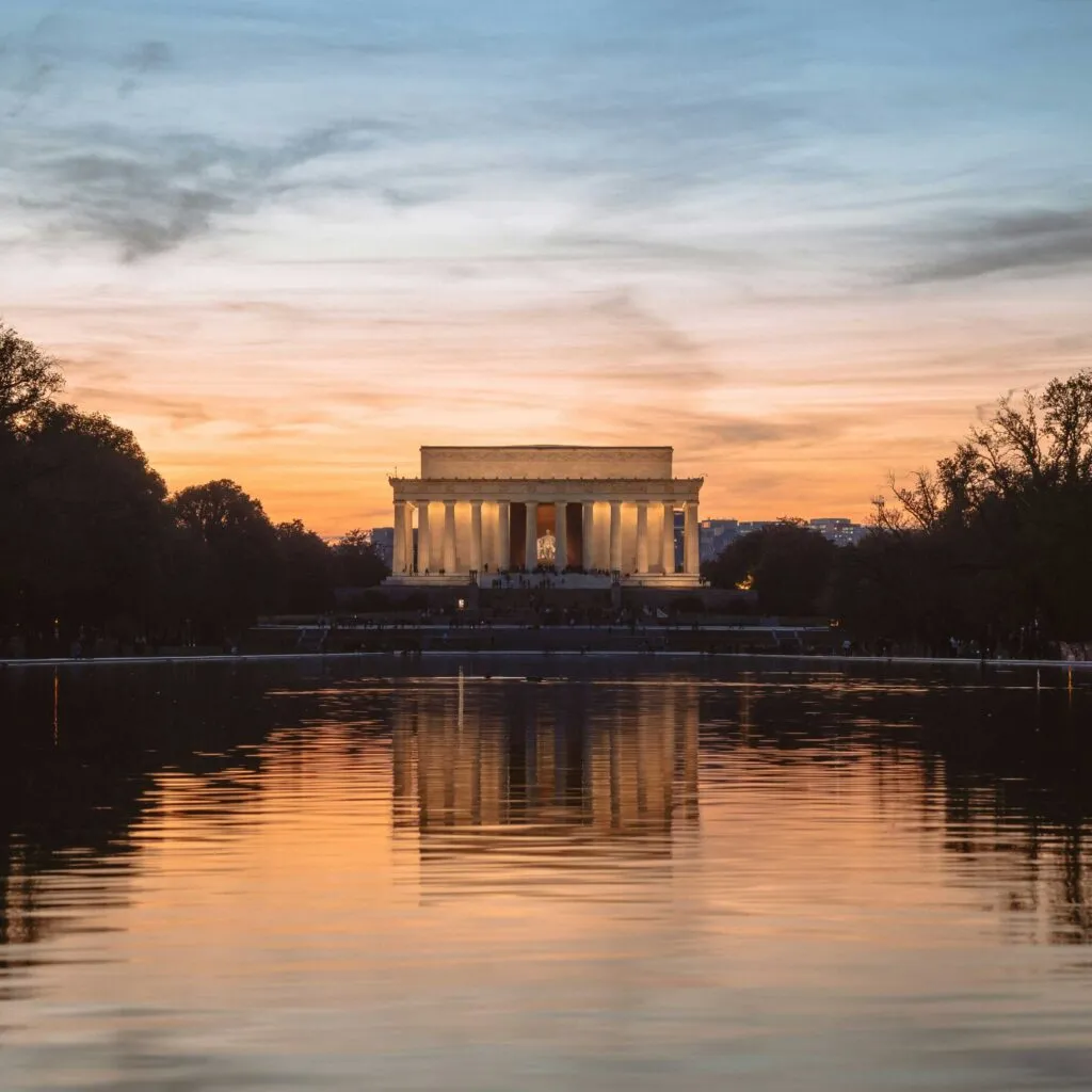 The Lincoln Memorial at sunset reflects on the calm waters of the National Mall's Reflecting Pool.
