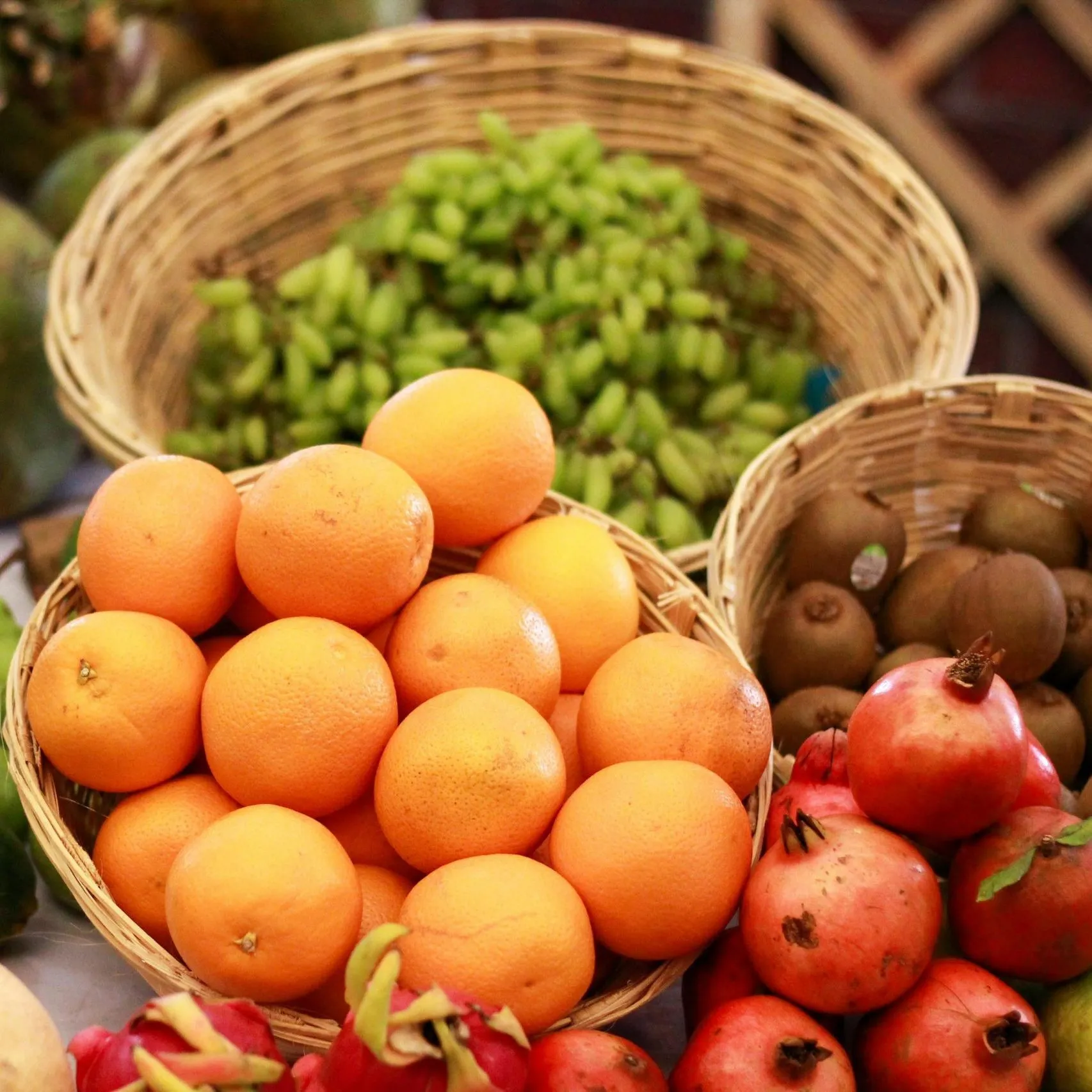 Baskets of oranges, grapes, kiwis, pomegranates, and dragon fruit arranged neatly at a market.