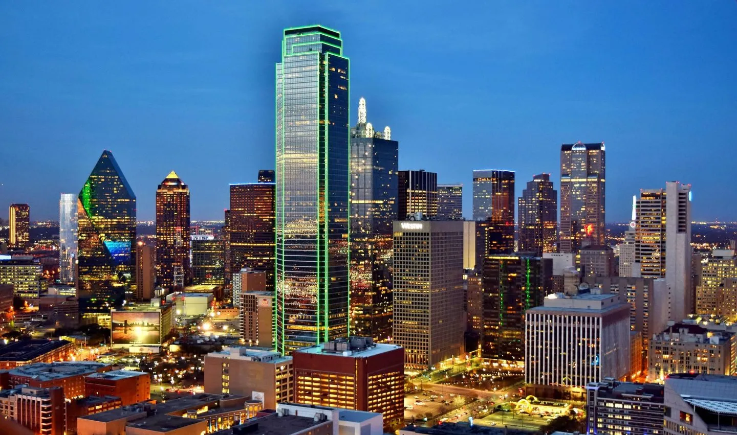 Dallas skyline at dusk featuring illuminated skyscrapers and vibrant city lights.