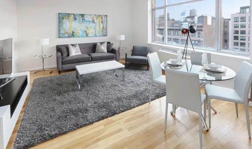 Modern living room with gray sofa, glass dining table, large window, and cityscape view.