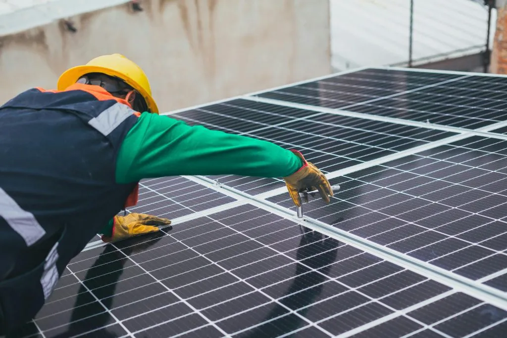 A worker in safety gear installs solar panels on a rooftop.