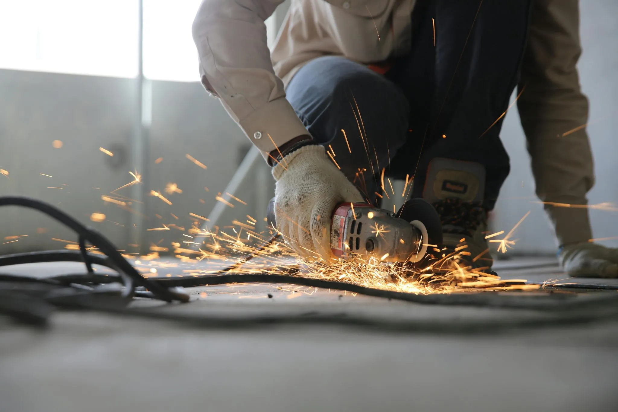 A worker uses an angle grinder, producing sparks while cutting metal on a construction site.