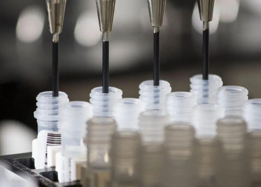 Automated pipettes dispense liquid into labeled test tubes in a laboratory setting.