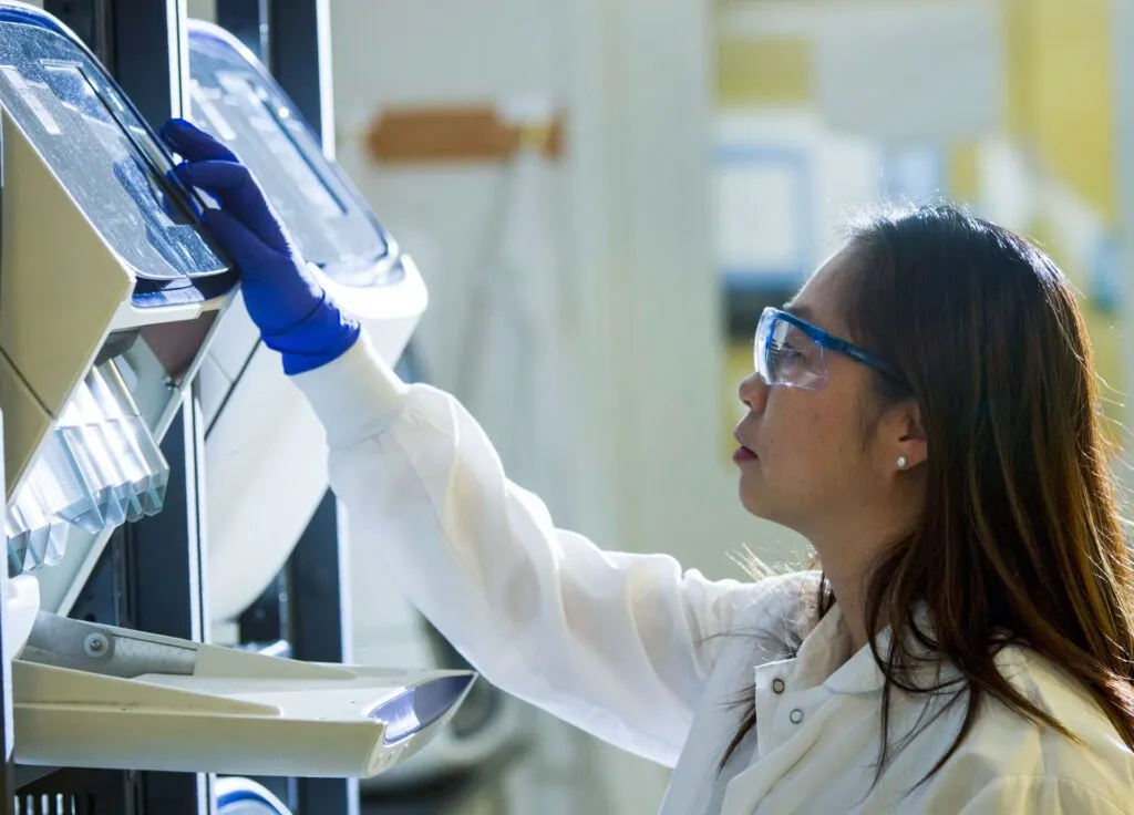 A lab technician operates advanced scientific equipment while wearing gloves and a lab coat.