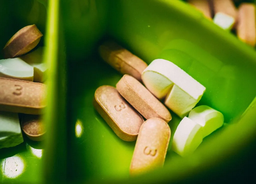 A close-up of assorted pills in a green compartmentalized container.