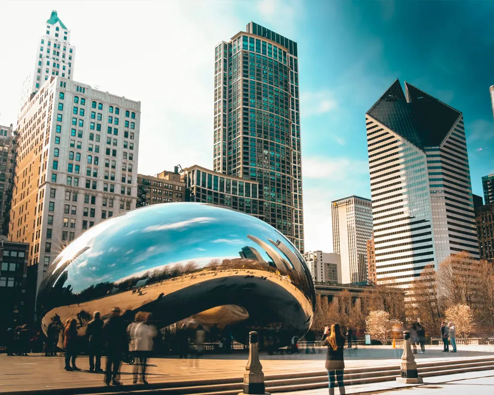 Cloud Gate sculpture in Chicago's Millennium Park, surrounded by skyscrapers and visitors.