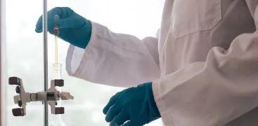 A scientist wearing gloves conducts a liquid transfer using laboratory glassware and clamps.
