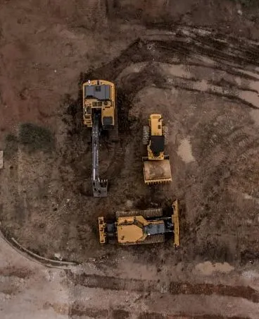 Aerial view of three construction vehicles on a dirt site with visible tire tracks.