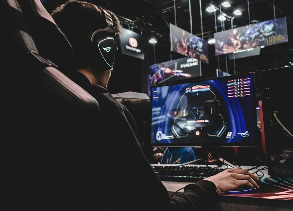 A gamer wearing headphones plays a video game on a PC at an esports event or gaming convention.