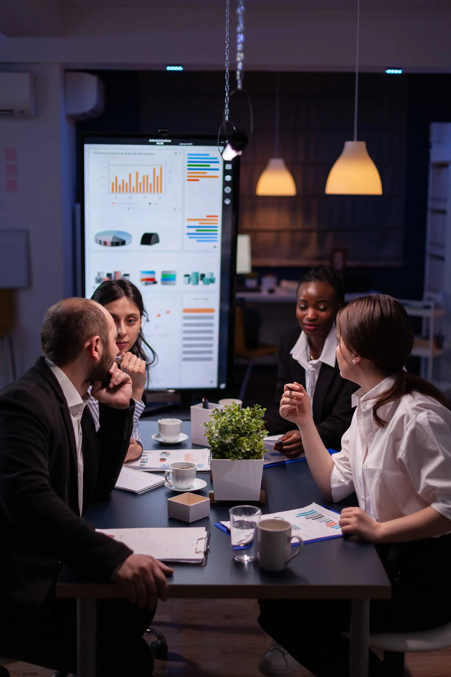 A team collaborates in a modern office, analyzing data displayed on a large screen.