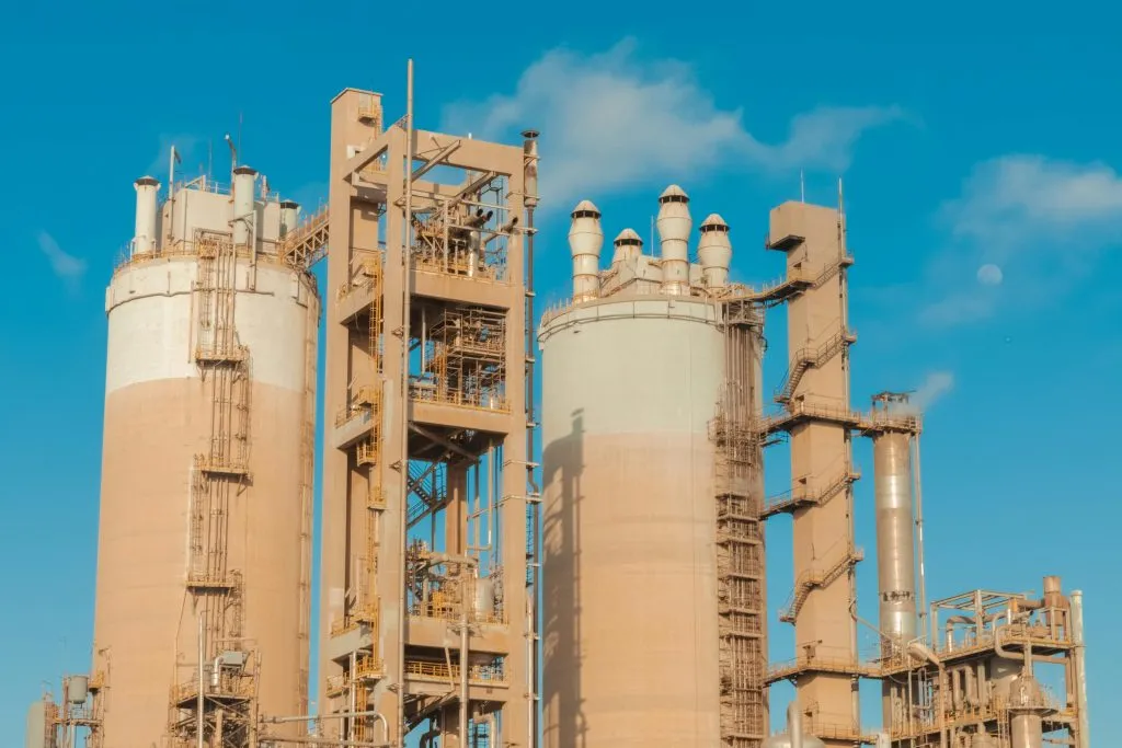Industrial facility with large silos, chimneys, and metal structures under a clear blue sky.