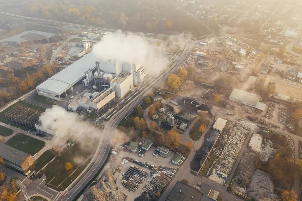 An industrial facility emits smoke, surrounded by construction sites and urban infrastructure.