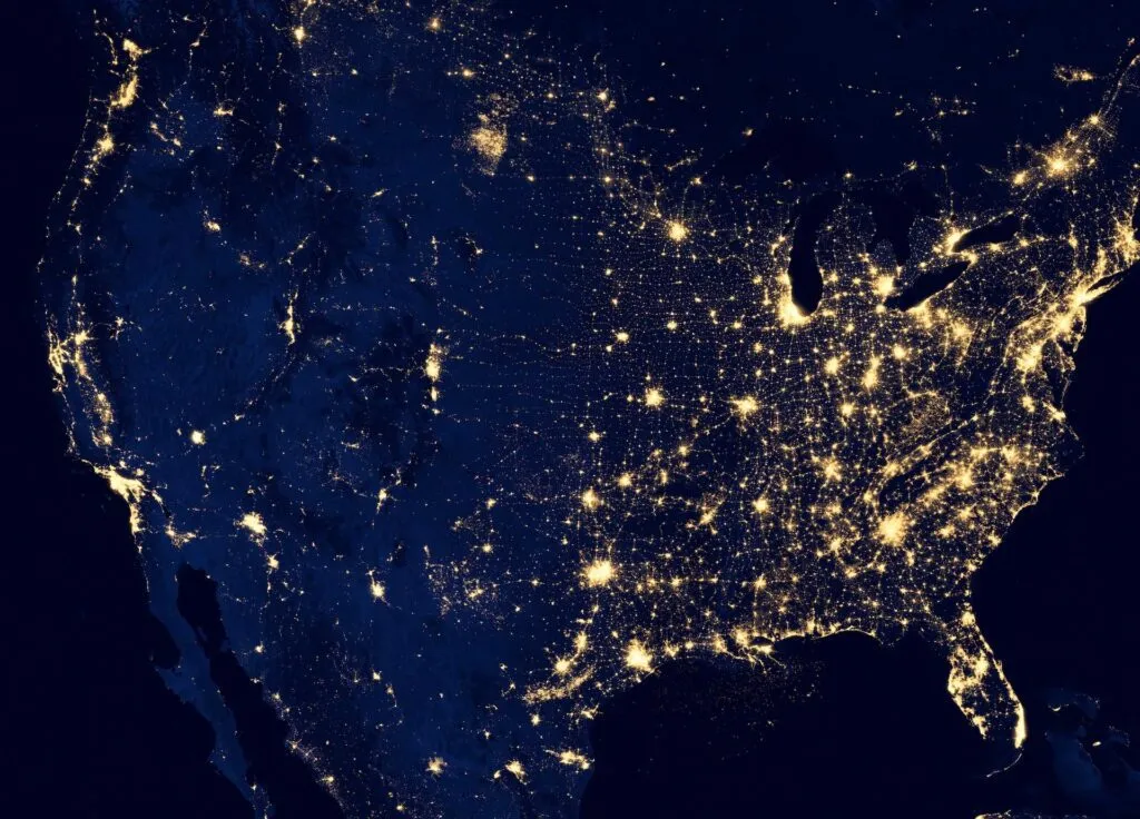 Satellite view of the U.S. at night, showing illuminated cities and infrastructure networks.