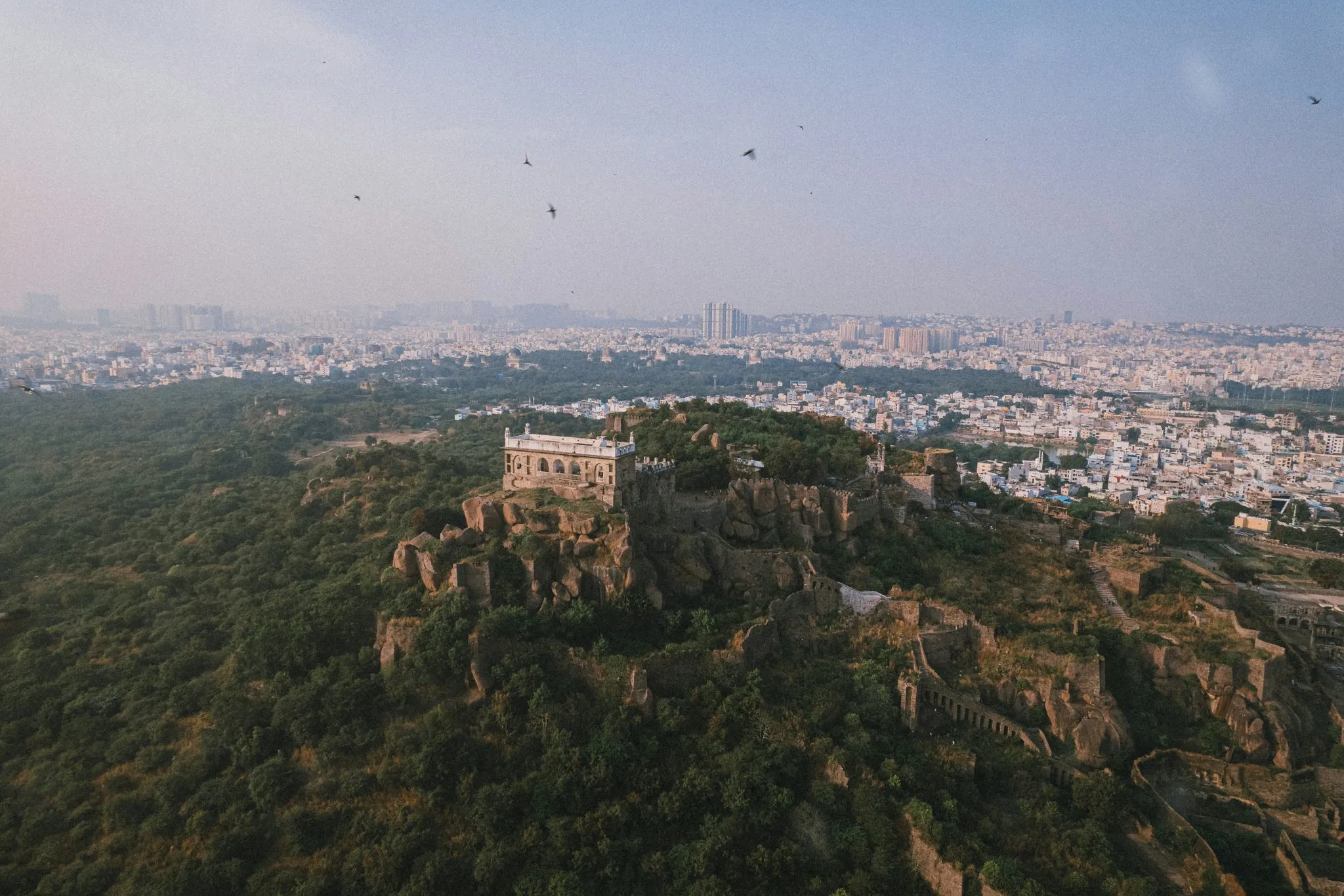 Aerial view of Golconda Fort surrounded by greenery, with Hyderabad cityscape in the background.
