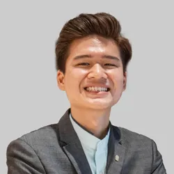 A person in formal attire with neatly styled hair, wearing a gray suit and light shirt.