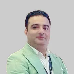 A person wearing a light green blazer and white shirt, accessorized with a lanyard.