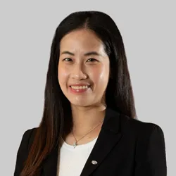 A woman with long dark hair wears a black blazer, white top, and a delicate necklace.