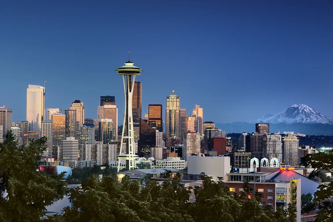 Seattle skyline at dusk, featuring the Space Needle and Mount Rainier in the background.