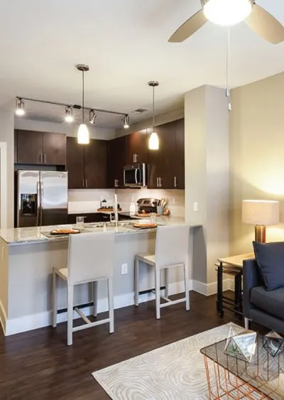 Modern kitchen with dark cabinets, pendant lighting, and a small dining area with bar stools.