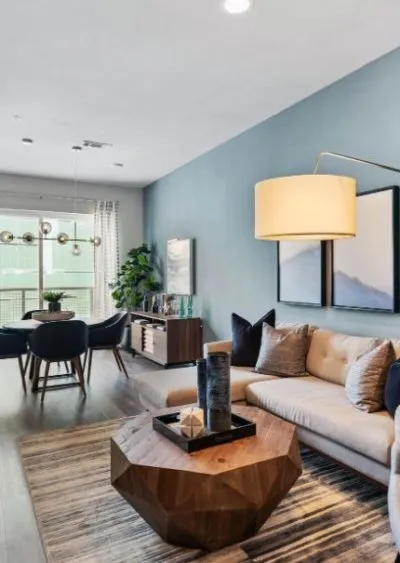Modern living room with blue walls, geometric wood table, and stylish dining area in the background.