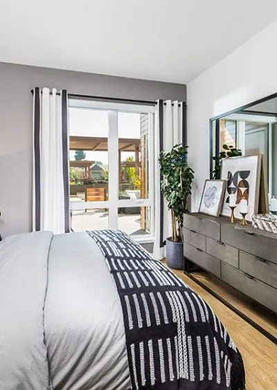 Modern bedroom with gray accents, large window, dresser, decor, and indoor plant.