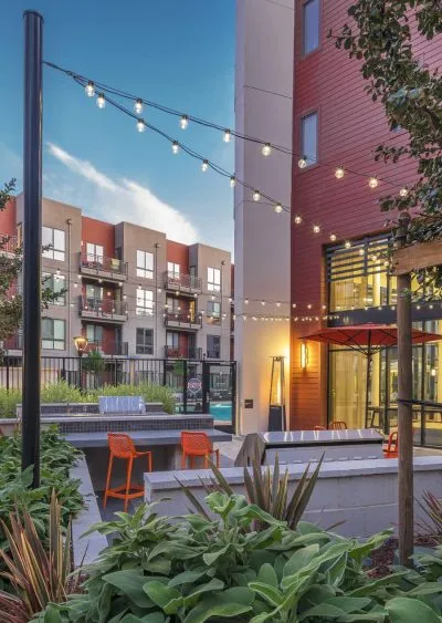 Modern apartment courtyard with string lights, seating, greenery, and contemporary architecture.