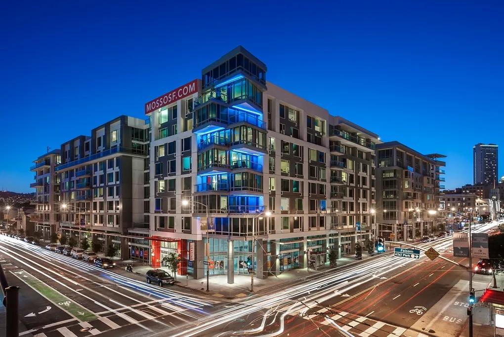 Modern urban apartment complex illuminated at night, located at a busy city intersection.