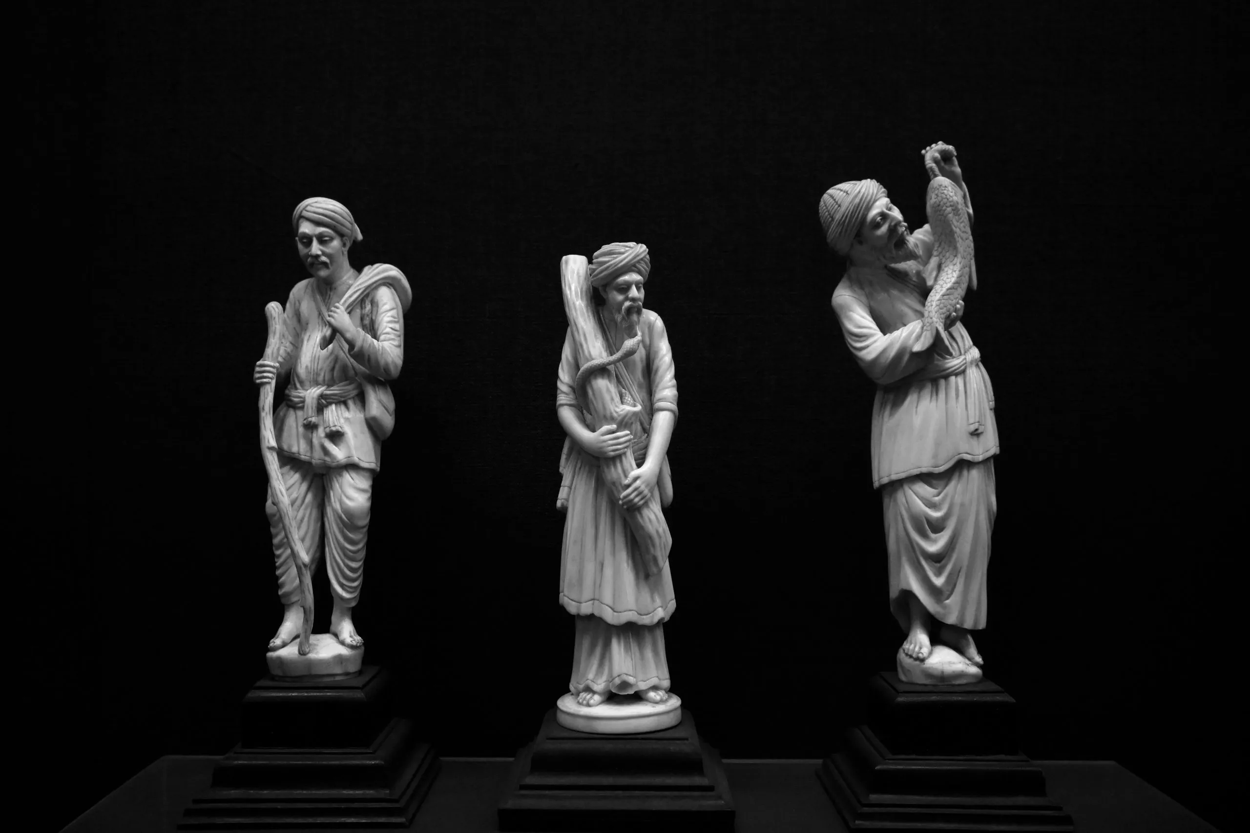 Three intricately carved statues depict figures in traditional attire, each holding distinct objects.