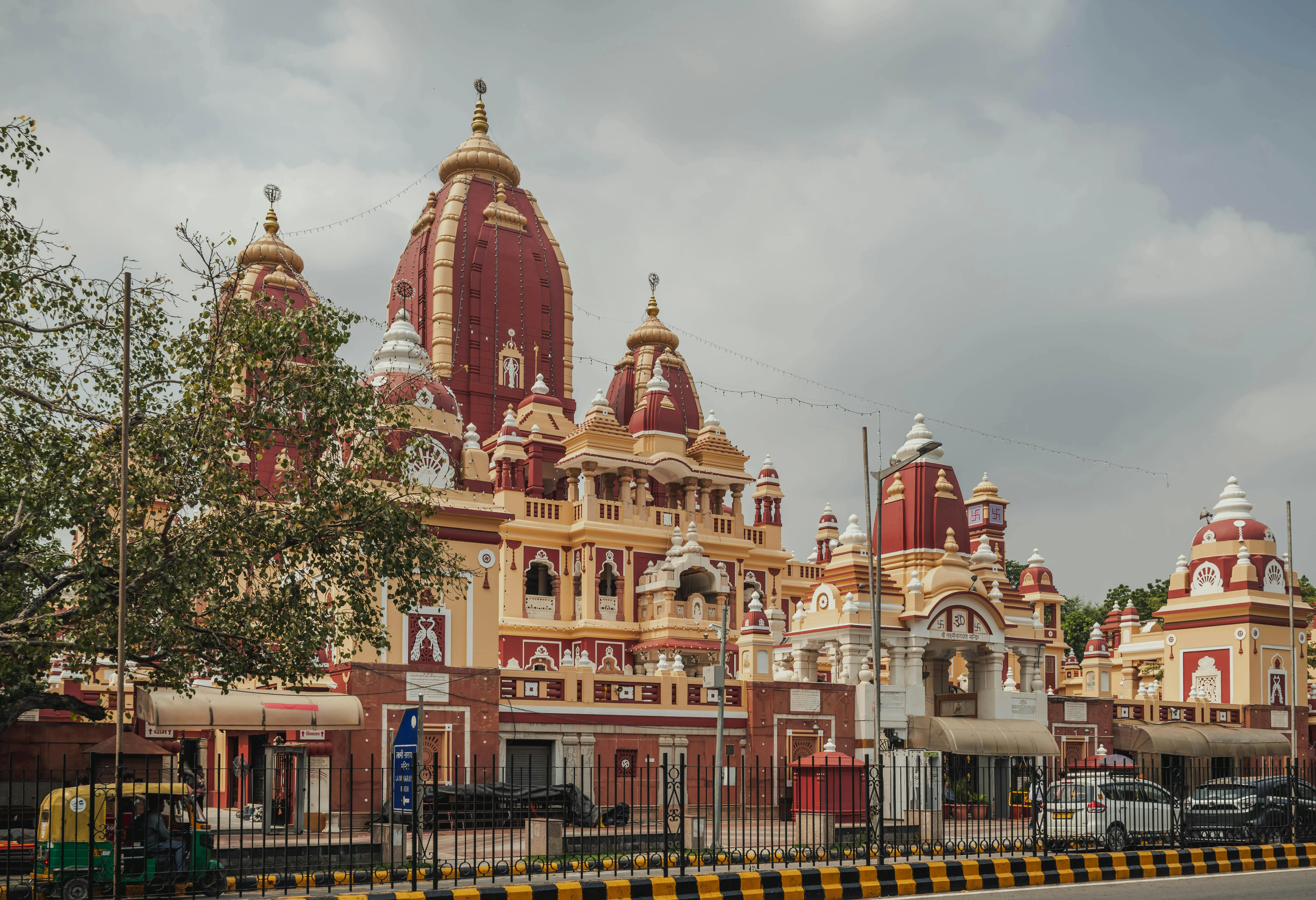A grand Hindu temple with ornate architecture, red and yellow domes, and surrounding urban elements.