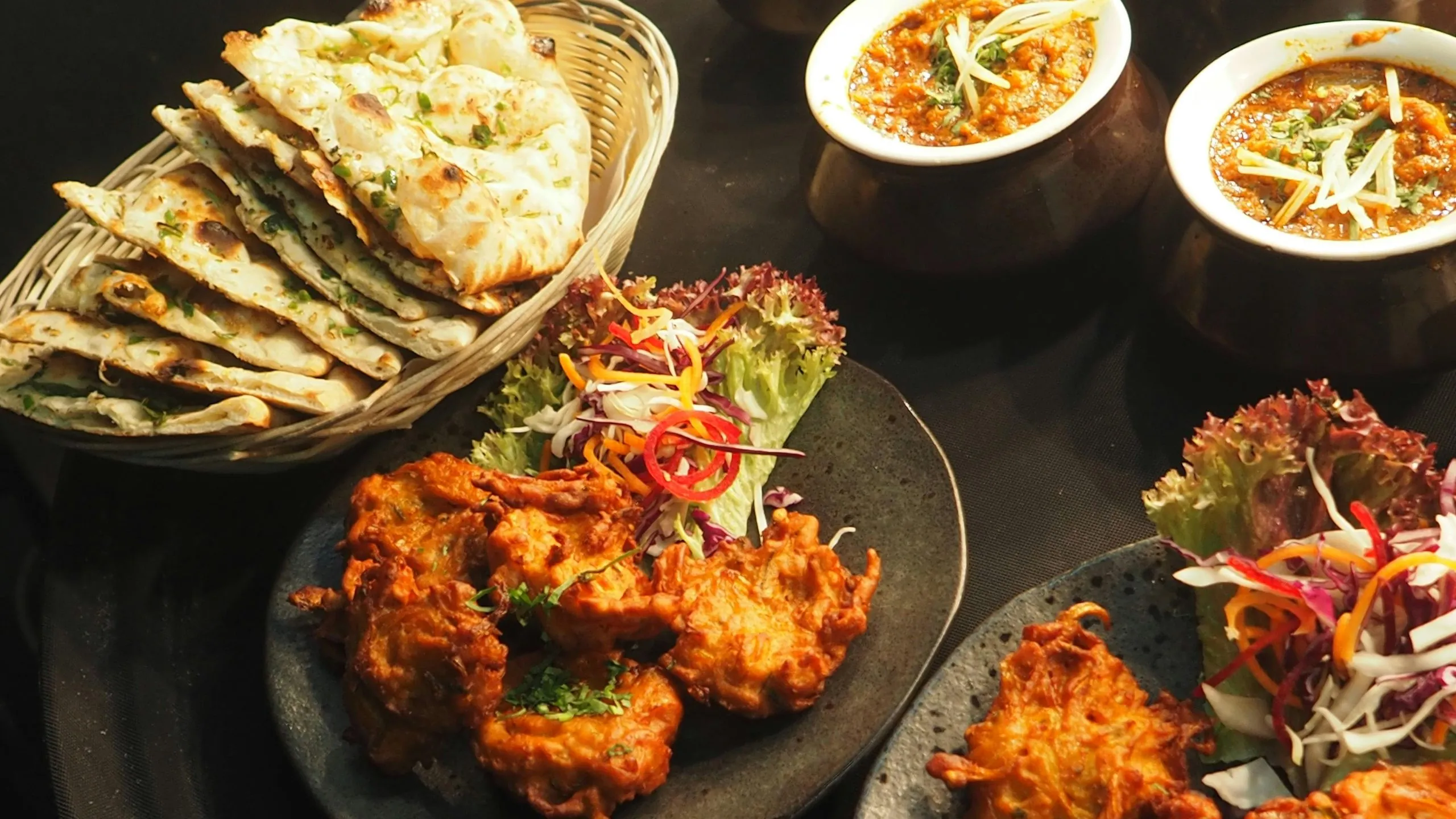 A spread of Indian cuisine featuring naan, curry, pakoras, and fresh salad garnished with herbs.