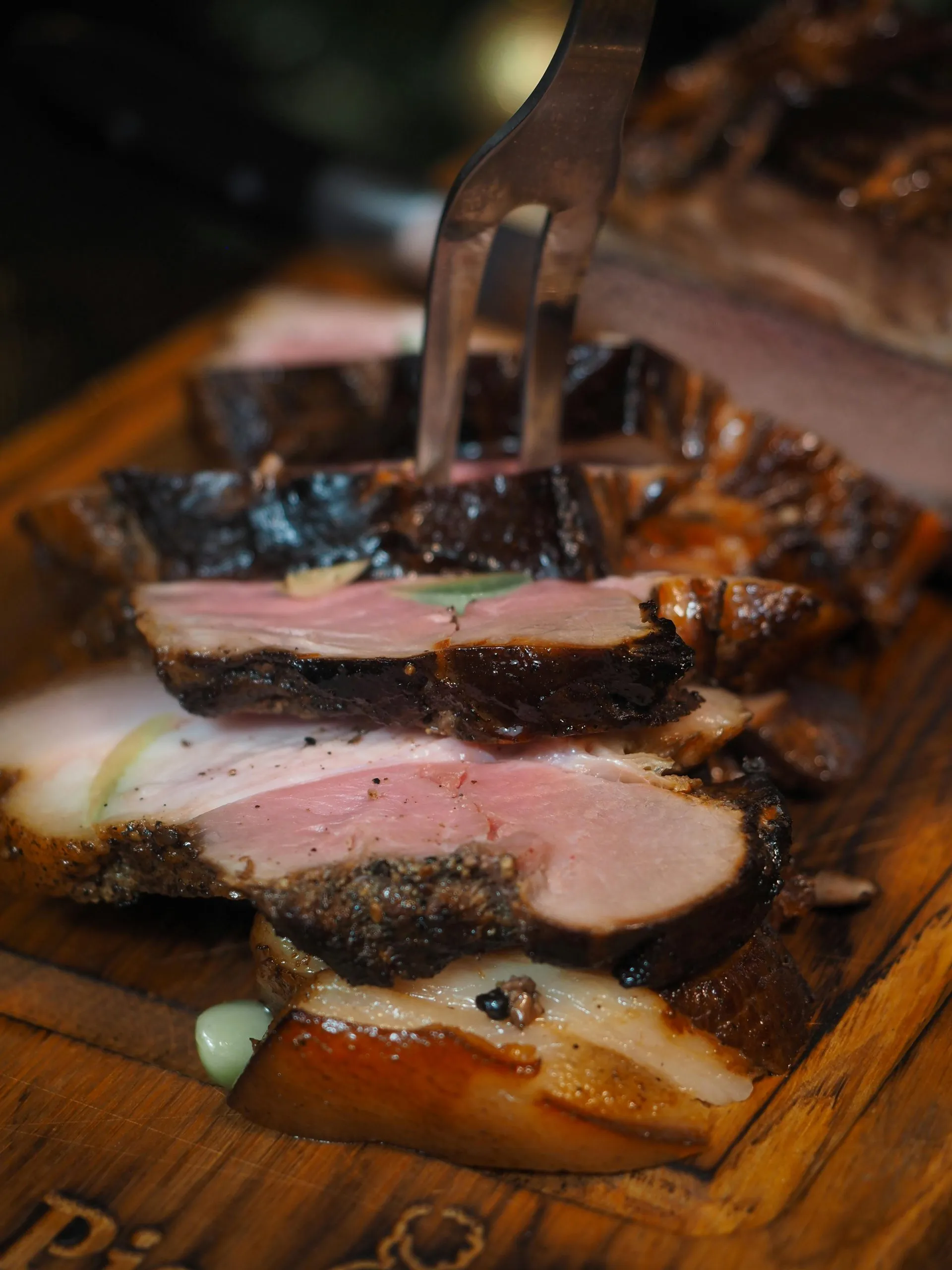 Slices of medium-rare meat on a wooden board, pierced by a fork, showcasing a juicy texture.