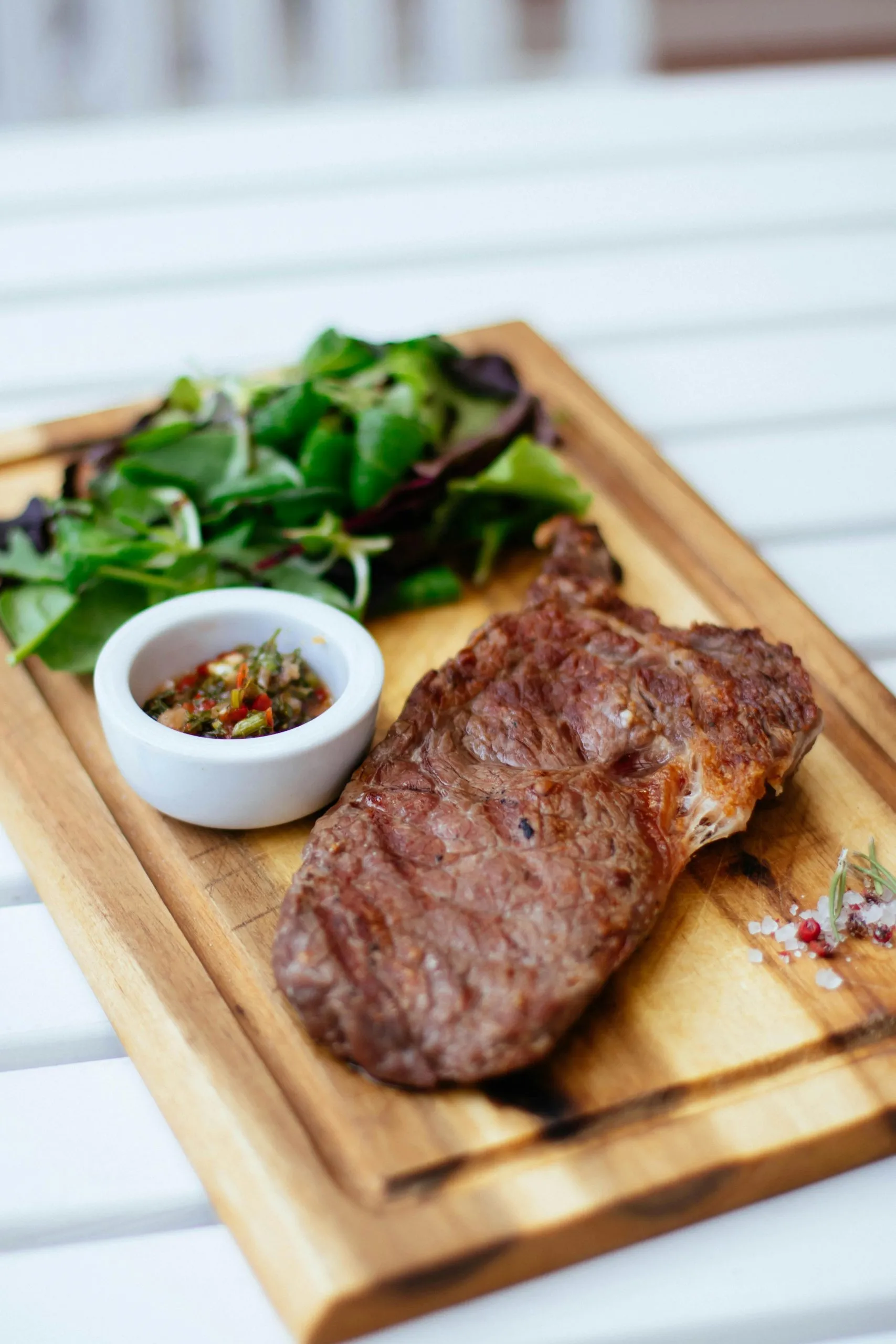 Grilled steak with salad and dipping sauce served on a wooden board.