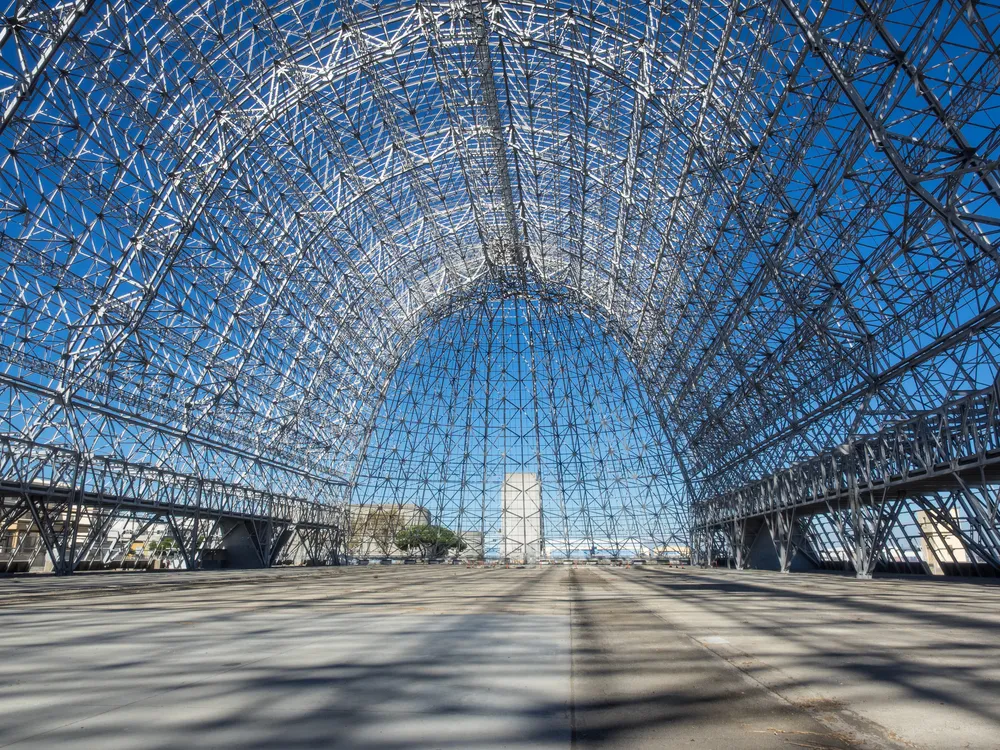 A vast steel framework forms an arched structure under a clear blue sky.
