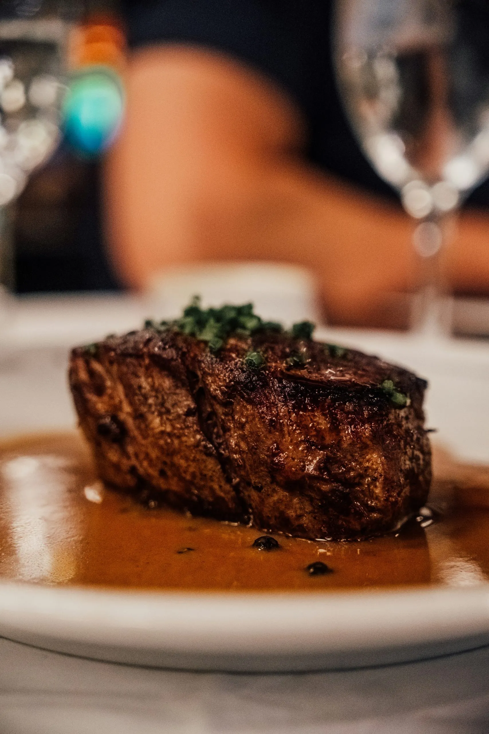 A seared steak topped with herbs, served in a rich brown sauce on a white plate.