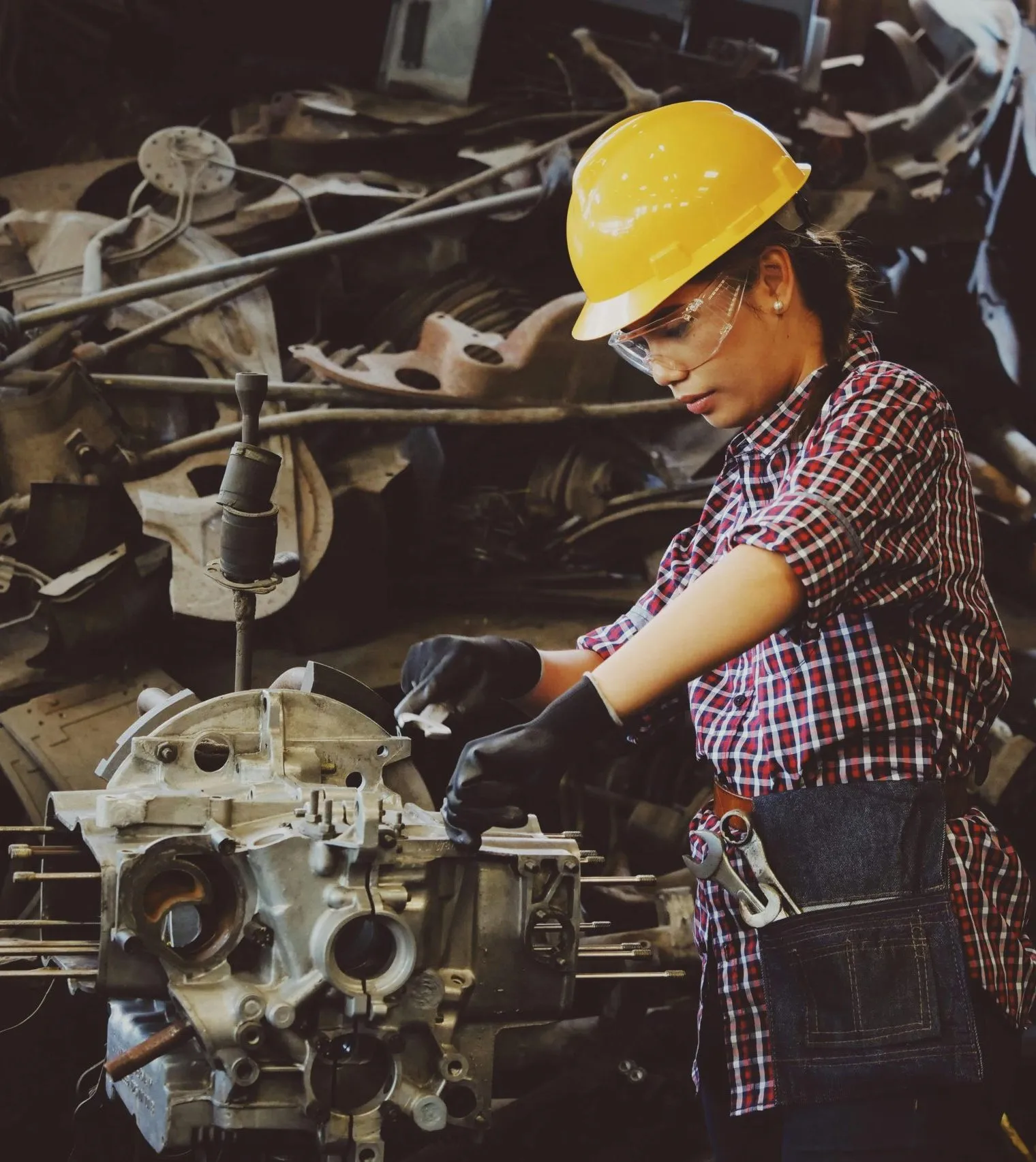A worker in a hard hat and gloves repairs machinery in an industrial setting.