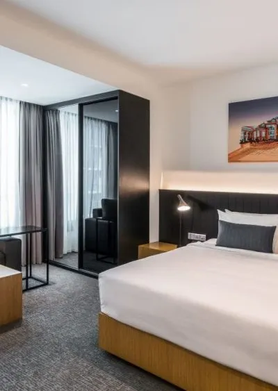 Modern hotel room with a sleek design, featuring a bed, seating area, and neutral tones.