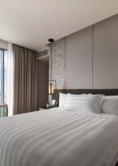 Modern hotel room with a neatly made bed, pendant light, and floor-to-ceiling window.
