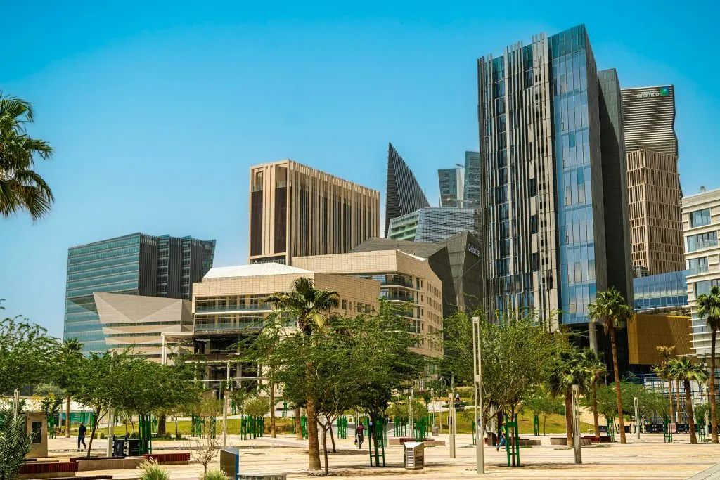 Modern skyscrapers and lush greenery in a vibrant urban business district under a clear blue sky.