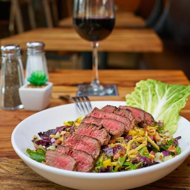 A plated steak salad with wine, set on a wooden table in a cozy dining setting.