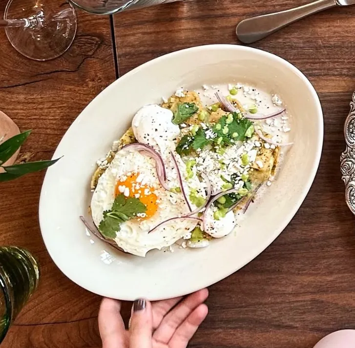 A plated dish featuring fried eggs, garnished with cilantro, red onion, cheese, and green sauce.