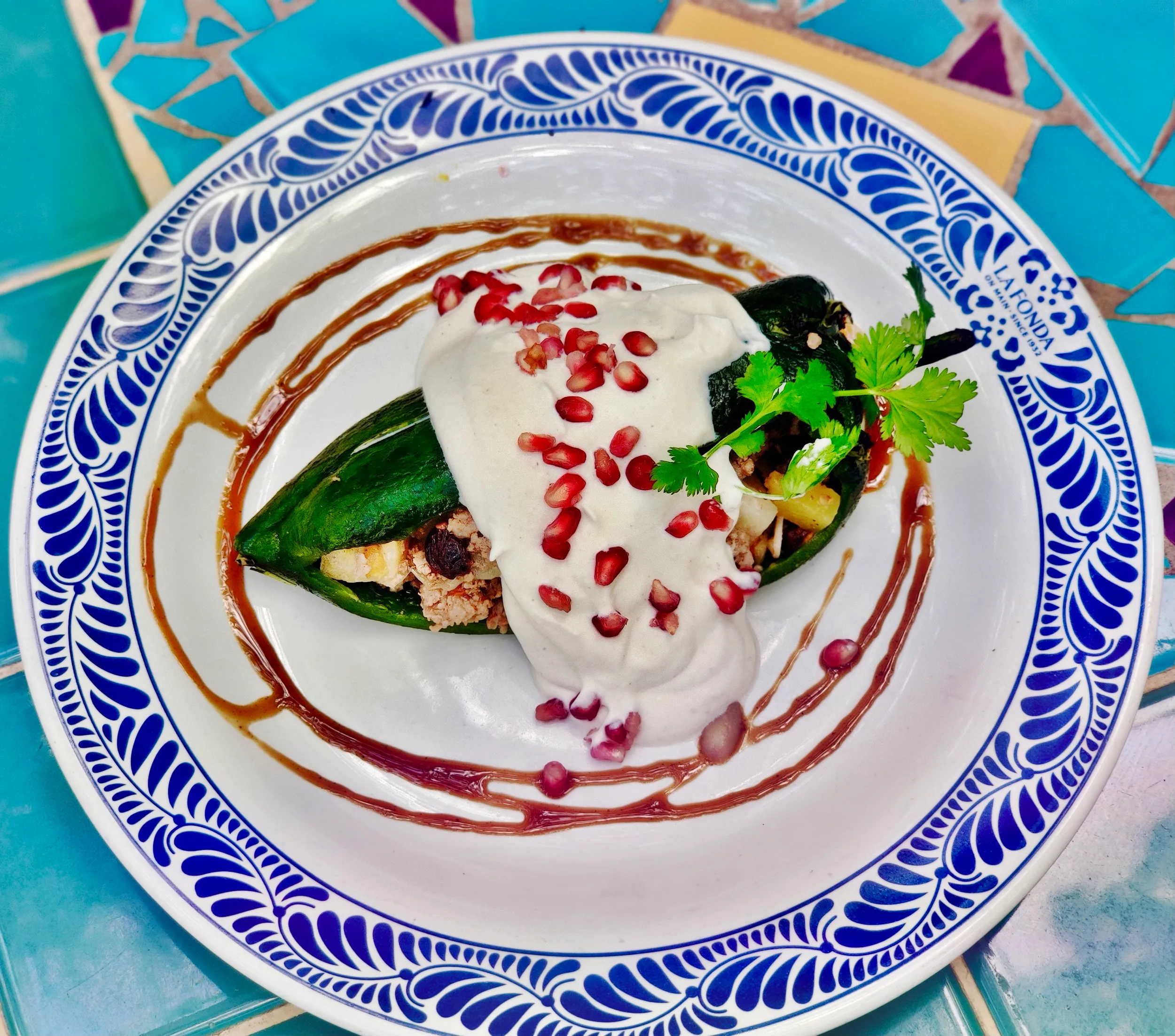 A plated chile en nogada garnished with pomegranate seeds and cilantro on a decorative dish.