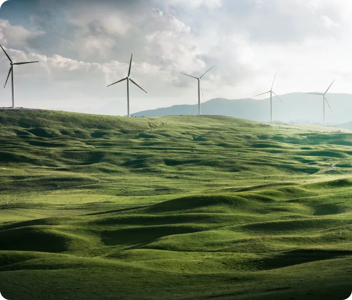 Wind turbines stand on rolling green hills under a cloudy sky, symbolizing renewable energy.
