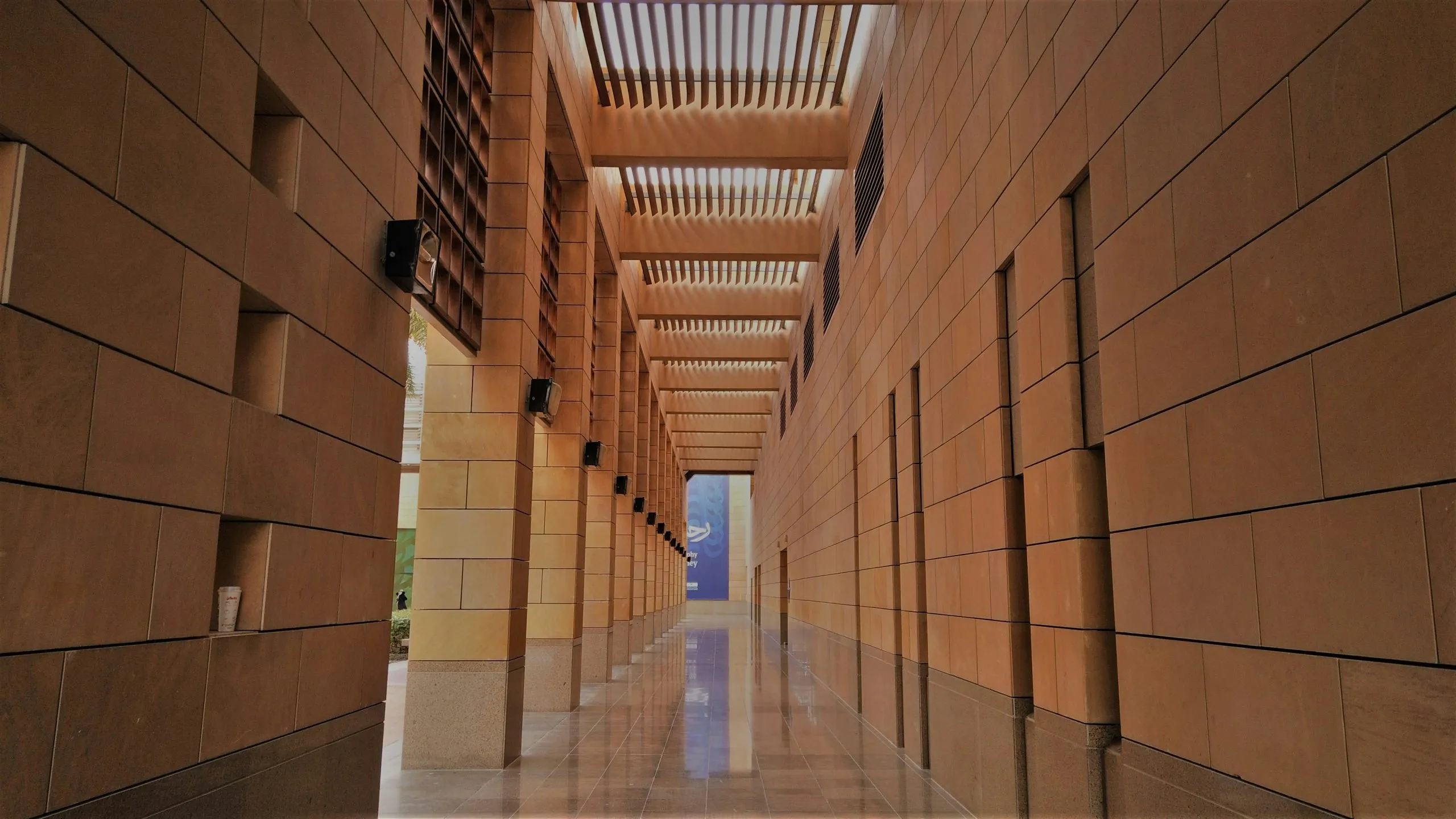 A symmetrical corridor with beige walls, wooden slats, and reflective flooring.