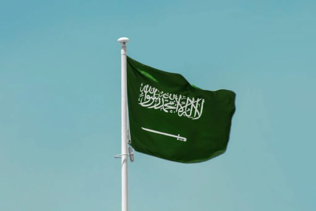 The Saudi Arabian flag features a green field with white Arabic script and a sword below it.