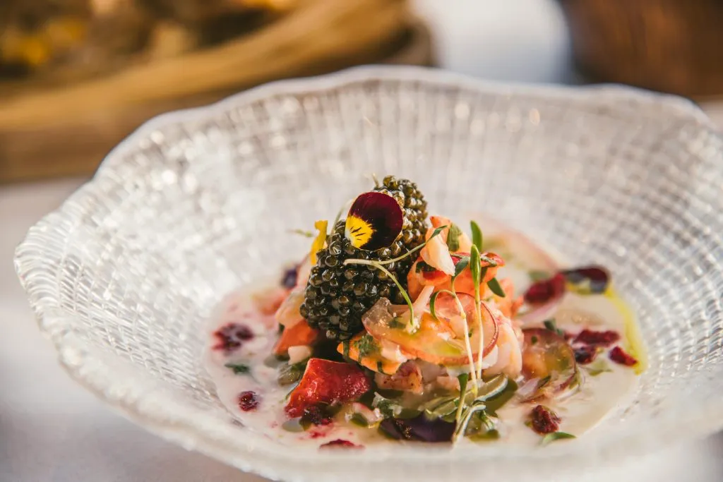 A gourmet seafood dish garnished with caviar, edible flowers, and microgreens in a glass bowl.