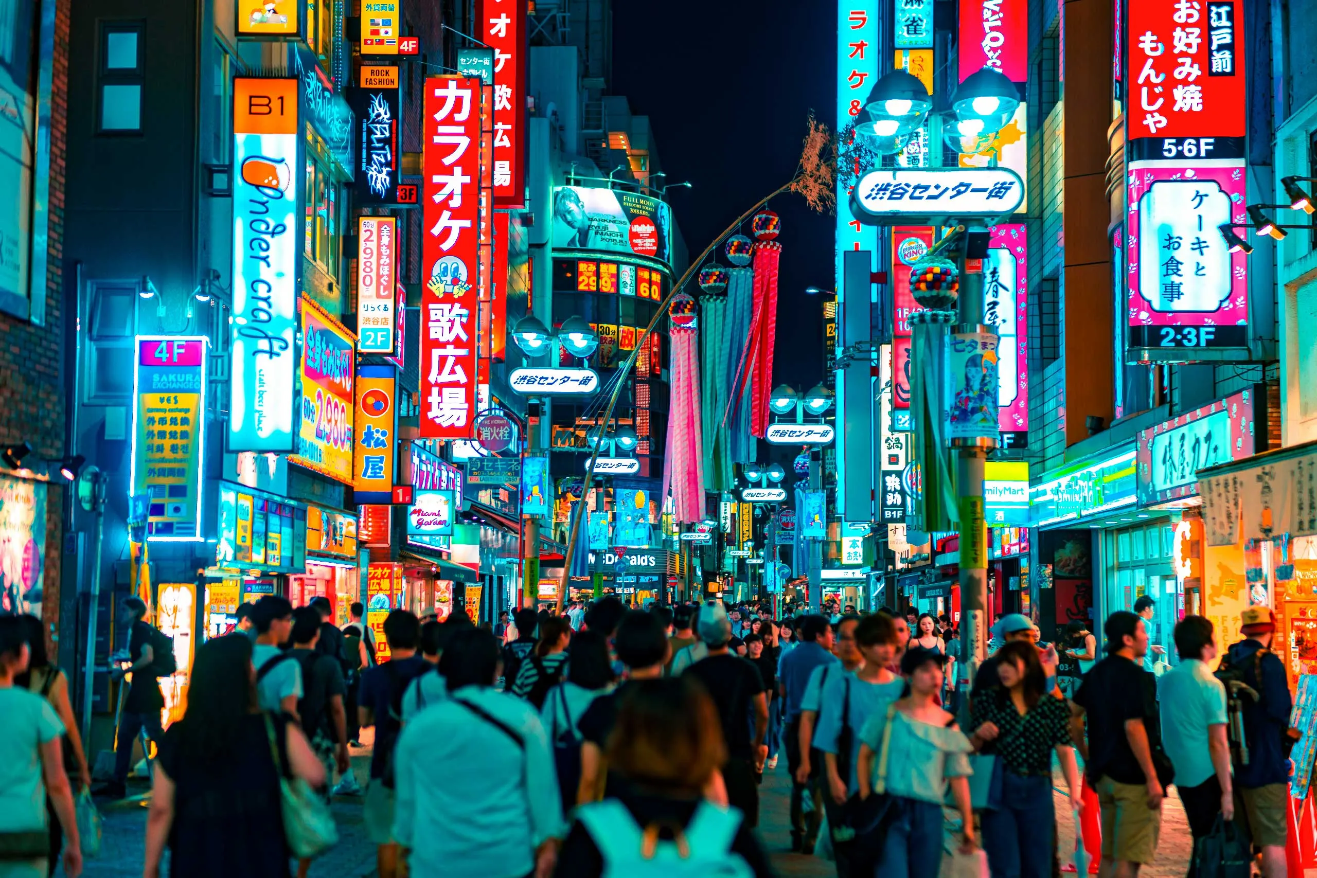 A vibrant, bustling Japanese street at night, illuminated by colorful neon signs and advertisements.