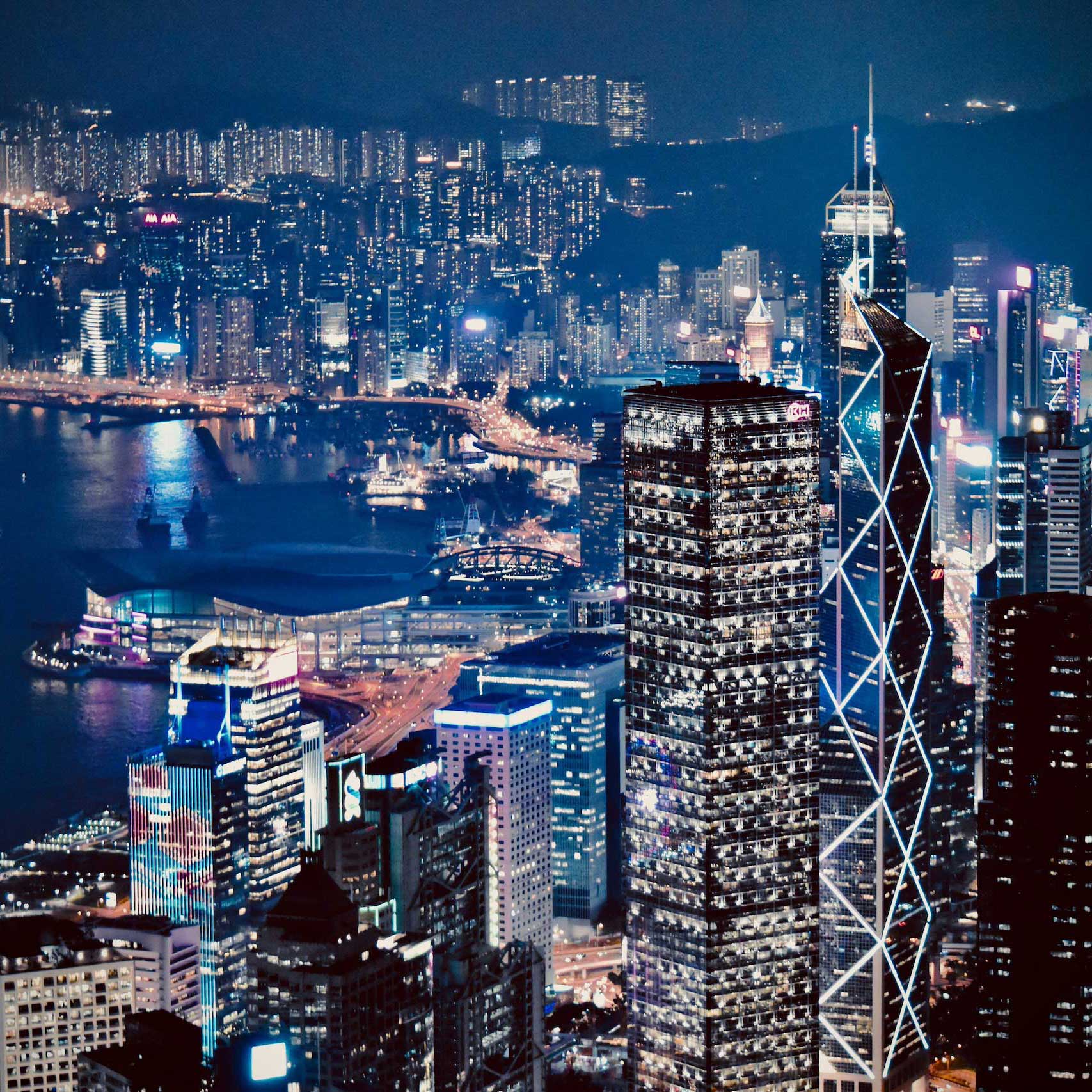 A vibrant cityscape at night featuring illuminated skyscrapers and a bustling harbor.